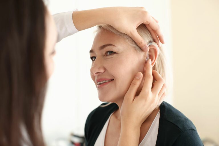 Audiologist placing hearing aid in woman's ear.